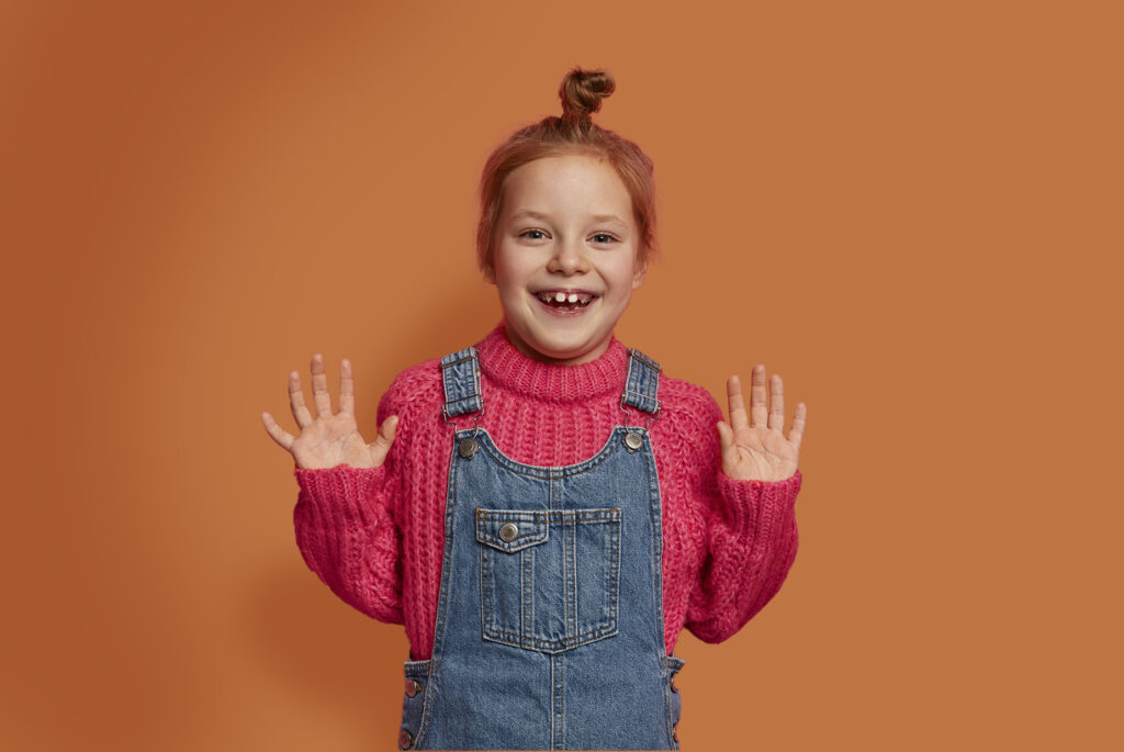 excited young girl with a big smile wearing a pink sweater overalls