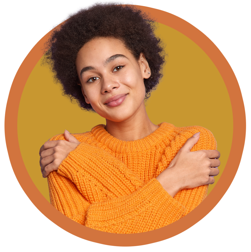 Women with curly black hair and an orange sweater giving herself a hug