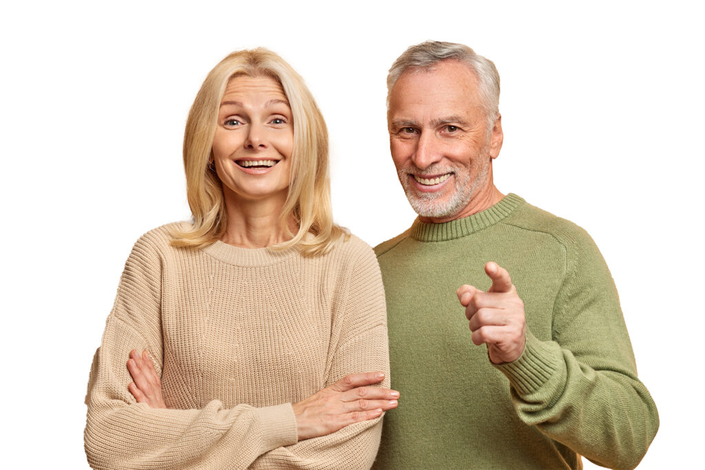 Portrait of happy aged woman and man stand closely to each other dressed in casual jumpers look with great interest in front isolated over brown studio background.